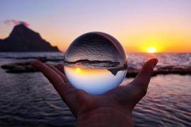 На картинке человек держит на ладони стеклянный шар, через который картина моря видится перевернутой вверх дном, как символ относительности добра и зла.