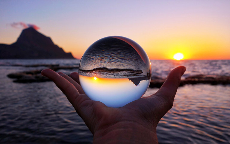 На картинке человек держит на ладони стеклянный шар, через который картина моря видится перевернутой вверх дном, как символ относительности добра и зла.