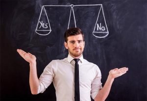 Мужчина стоит на фоне черной доски с изображением весов, на которых написано YES и No (Да или нет)