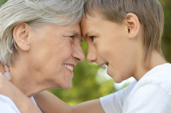 Внук и бабушка с улыбками на лицах обнимают друг друга, радостные от того, что могут выразить свою любовь
