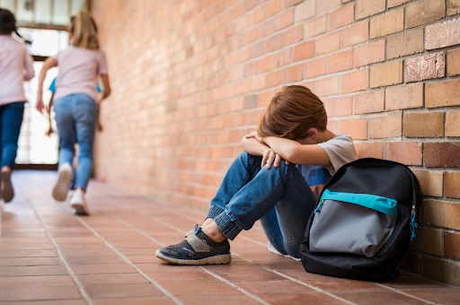 На картинке мальчик сидит на полу у стены один и плачет, а равнодушные дети пробегают мимо, у ребенка явные проблемы общения со сверстникам