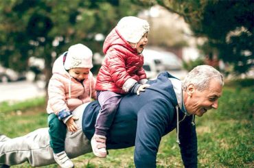 На фотографии счастливый пожилой мужчина делает физические упражнения - отжимается - с сидящими на его спине детьми. Его жизнь прошла в исканиях славы, и только став дедушкой, он, наконец понял, что главная жизненная ценность - это семья.